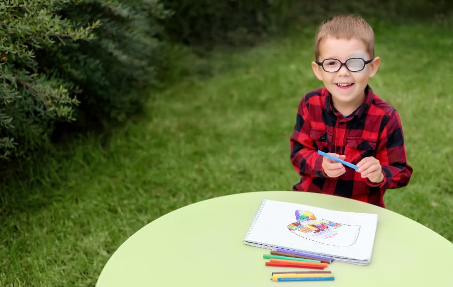 Child wearing glasses and eye patch drawing in garden