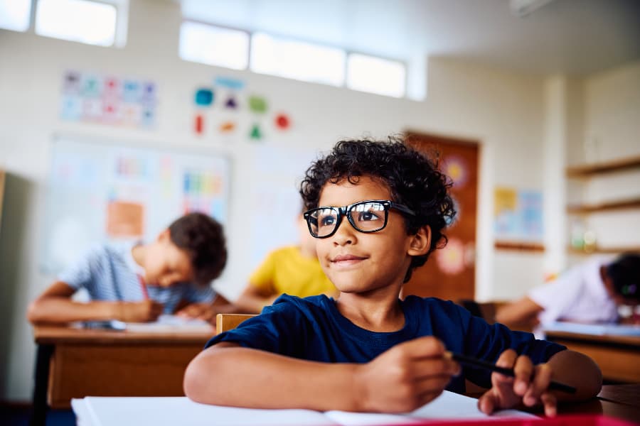 Young boy wearing glasses sitting at classroom desk